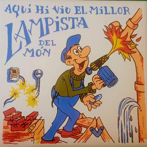 Rajola decorativa amb la inscripció 'AQUÍ HI VIU UN LAMPISTA' , amb un disseny tradicional i colors vius